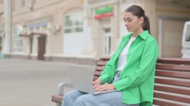 Busy Young Woman Using Laptop Sitting Outdoor on Bench