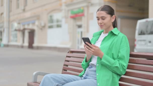 Young Woman Using Smartphone While Sitting Outdoor Bench — Vídeo de Stock