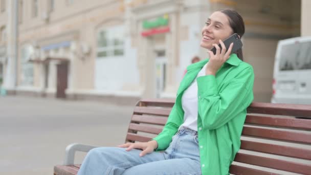 Молода Жінка Розмовляє Телефону Сидячи Відкритому Повітрі Лавці — стокове відео