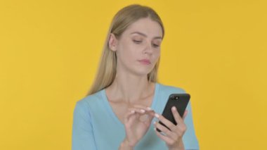 Casual Young Woman Celebrating on Smartphone on Yellow Background 