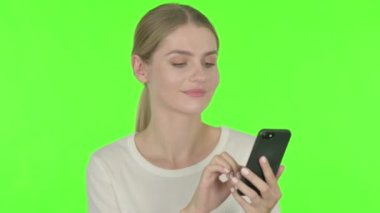 Casual Young Woman Browsing Smartphone on Green Background 
