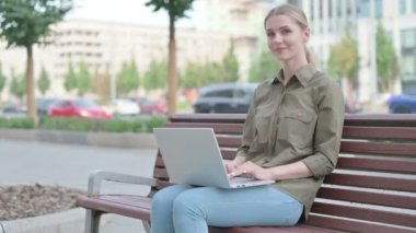 Young Woman with Laptop Smiling at Camera while Sitting Outdoor on Bench