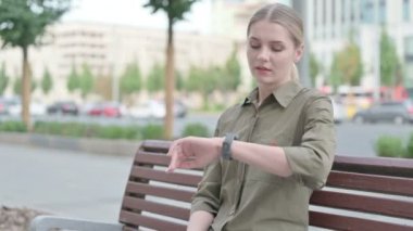 Outdoor Young Woman Checking Time while Waiting on Bench