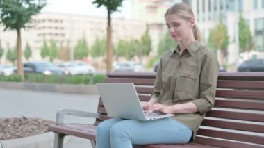 Young Woman with Laptop Showing Thumbs Up Sign While Sitting Outdoor on Bench 