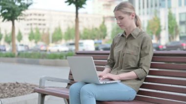 Young Woman Celebrating Success on Laptop while Sitting Outdoor on Bench