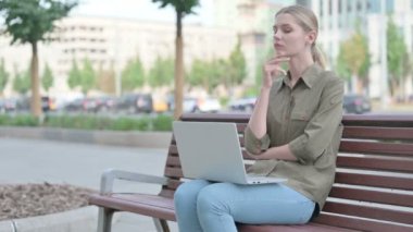 Thinking Young Woman Using Laptop while Sitting Outdoor on Bench