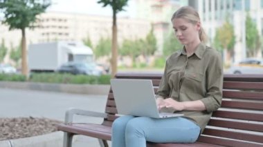 Young Woman with Wrist Pain Using Laptop while Sitting Outdoor on Bench