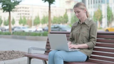 Young Woman with Neck Pain Using Laptop while Sitting Outdoor on Bench