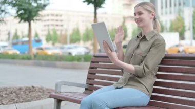 Online Video Chat on Tablet by Young Woman Sitting Outdoor on Bench 