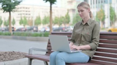 Distressed Young Woman with Headache Using Laptop while Sitting Outdoor on Bench
