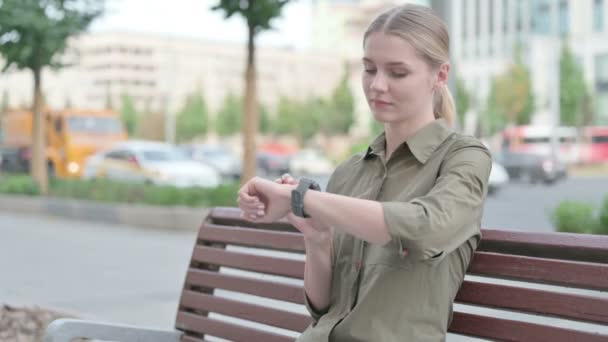 Young Woman Using Smartwatch While Sitting Outdoor Bench — Video
