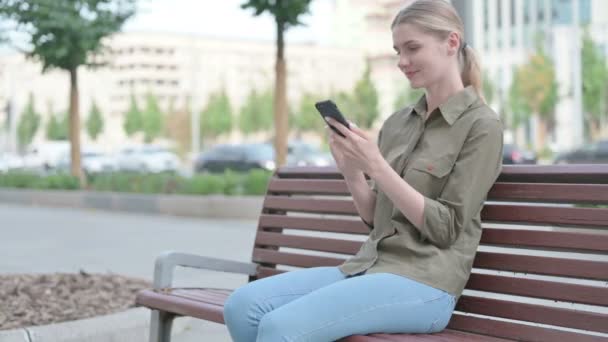 Young Woman Using Smartphone While Sitting Outdoor Bench — 图库视频影像