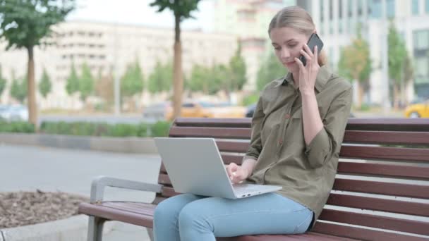 Young Woman Talking Phone Using Laptop While Sitting Outdoor Bench — Video