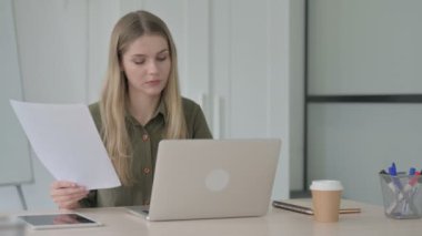 Blonde Young Woman Evraklar ve Laptop üzerinde çalışıyor.