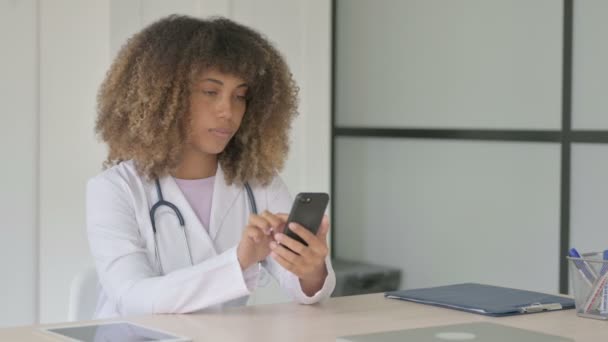 診療所に座っている間にスマートフォンを使っている女性アフリカ人医師 — ストック動画