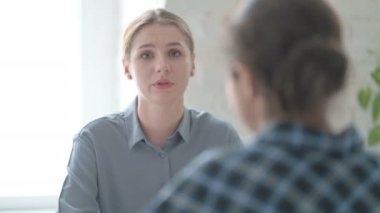 Genç sarışın kadın toplantı sırasında Hintli kadınla konuşuyor.