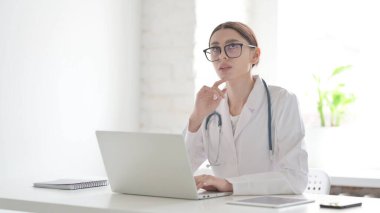 Ofiste dizüstü bilgisayarla çalışırken düşünen genç kadın doktor.