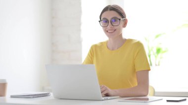 Ofiste dizüstü bilgisayar kullanırken Kameraya Gülümseyen Genç Kadın