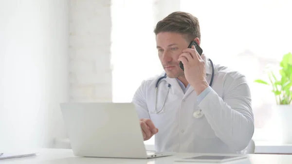 電話で話すノートパソコンを持つ中年医師 — ストック写真