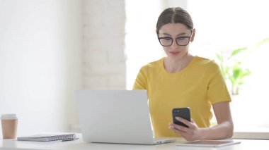 Ofiste dizüstü bilgisayar kullanırken Smartphone kullanan genç kadın