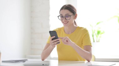 Ofiste akıllı telefon kullanan çekici genç kadın.