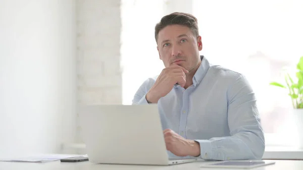Middle Aged Man Thinking while Working on Laptop in Office