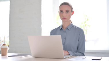 Ofiste dizüstü bilgisayar kullanırken Genç Kadın Kameraya Bakıyor