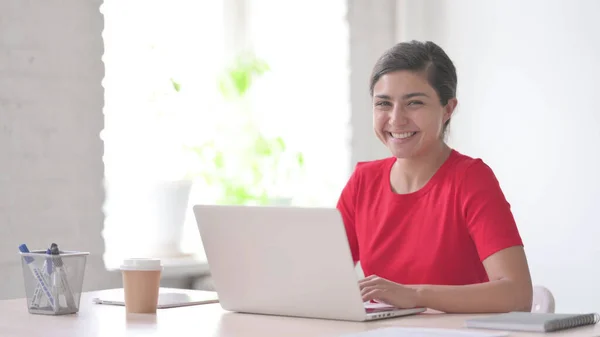 Young Indian Woman Smiling at Camera while using Laptop in Office