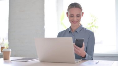 Ofiste dizüstü bilgisayar kullanırken Smartphone kullanan genç kadın