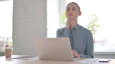 Ofiste dizüstü bilgisayar kullanırken boyun ağrısı çeken genç bir kadın.