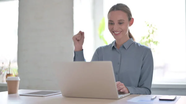 オフィスでノートパソコンを使いながら成功を祝う若い女性 — ストック写真