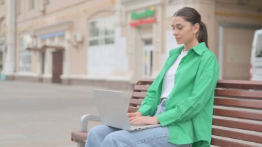 Busy Young Woman Using Laptop Sitting Outdoor on Bench