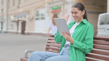 Online Video Chat on Tablet by Young Woman Sitting Outdoor on Bench