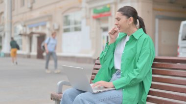 Coughing Young Woman Using Laptop while Sitting Outdoor on Bench