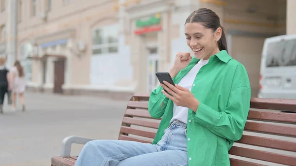Young Woman Celebrating Online Success Smartphone While Sitting Outdoor Bench — 图库照片