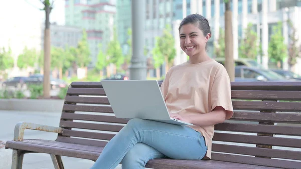 Young Indian Woman Smiling at Camera while using Laptop Outdoor