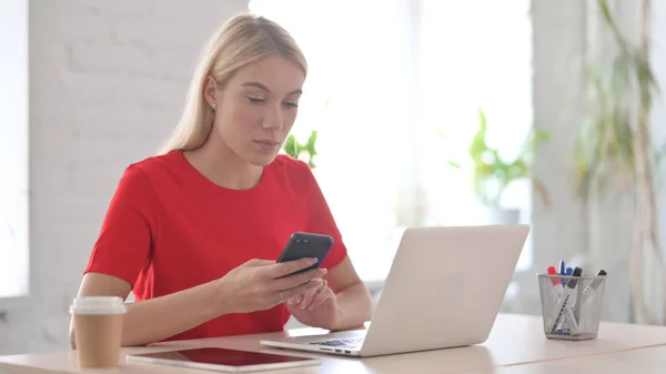 Young Woman Browsing Internet Smartphone While Using Laptop Office —  Fotos de Stock