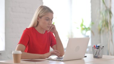 Ofiste dizüstü bilgisayarla çalışırken düşünen genç bir kadın.