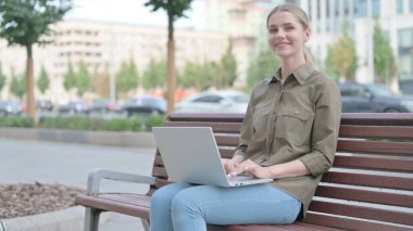 Young Woman with Laptop Smiling at Camera while Sitting Outdoor on Bench