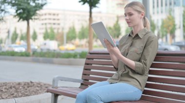 Young Woman using Tablet while Sitting Outdoor on Bench