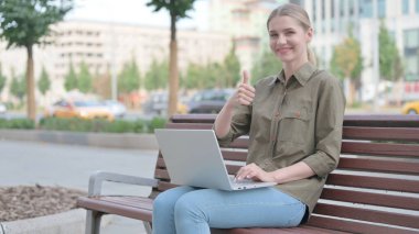 Young Woman with Laptop Showing Thumbs Up Sign While Sitting Outdoor on Bench