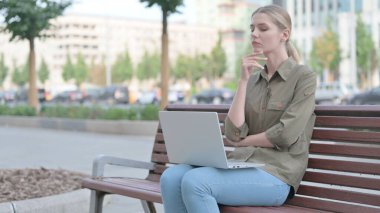 Thinking Young Woman Using Laptop while Sitting Outdoor on Bench