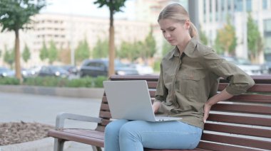 Young Woman with Back Pain Using Laptop while Sitting Outdoor on Bench