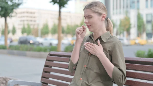 Sick Young Woman Coughing while Sitting on Bench Outdoor