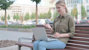 Young Woman Talking on Video Call while Sitting Outdoor on Bench