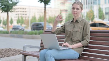 Thumbs Down by Young Woman with Laptop Sitting on Bench
