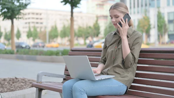 Молода Жінка Розмовляє Телефону Використовує Ноутбук Сидячи Відкритому Повітрі Лавці — стокове фото
