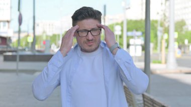 Orta yaşlı bir adamın açık havada başı ağrıyan portresi