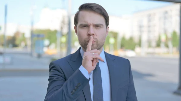 Outdoor Portrait of Businessman with Finger on Lips, Please be Quiet