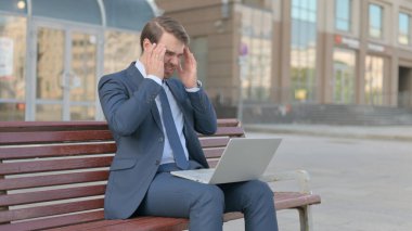 Middle Aged Businessman with Headache Using Laptop while Sitting Outdoor on Bench